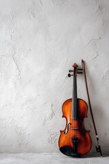 A violin with a bow rests against a textured white wall its wooden body contrasting with the stark background