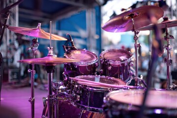 Fototapeta premium Closeup shot of a drum set illuminated with purple and pink lighting on what seems like a concert stage
