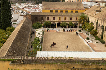 An aerial view of the Royal Stables of Cordoba, showcasing a sandy equestrian arena with riders and...