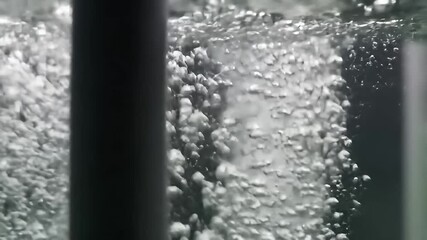 Many air bubbles rise in water. Grey pipe runs vertically to the left of frame - Powered by Adobe