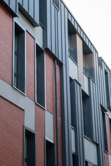 A brick building with a black roof. The building has a lot of windows. The windows are rectangular and are of different sizes