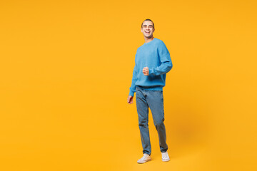 Fototapeta premium Full body young smiling happy middle eastern man he wearing blue sweatshirt casual clothes walking going looking camera isolated on plain yellow orange background studio portrait. Lifestyle concept.