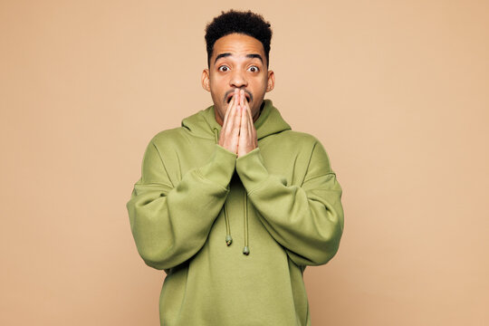 Young shocked surprised man of African American ethnicity he wear green hoodie casual clothes cover mouth with hand isolated on plain pastel light beige background studio portrait. Lifestyle concept. - Powered by Adobe