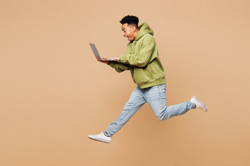 Full body young IT man of African American ethnicity wears green hoodie casual clothes jump high...