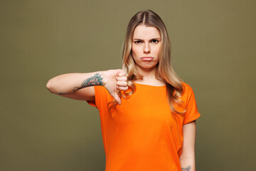Young sad disappointed displeased Caucasian woman wears orange t-shirt casual clothes showing thumb...