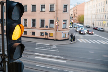 Yellow traffic light is activated at a city intersection where vehicles are moving and pedestrians...