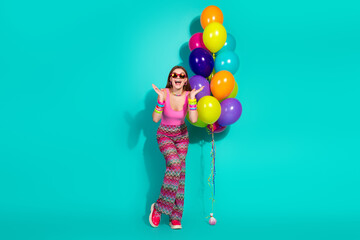 Stylish young woman holding colorful balloons against teal background showcasing retro fashion with...