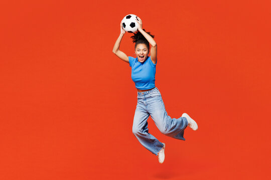 Full body young excited happy woman fan wears blue t-shirt cheer up support football sport team hold in hand catch soccer ball watch tv live stream jump high isolated on plain red orange background. - Powered by Adobe