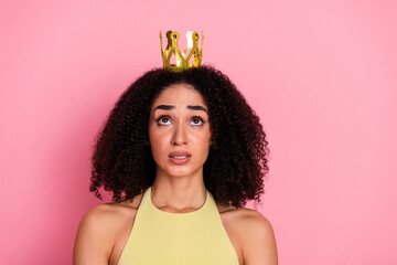 Charming young woman in a yellow dress wearing a golden crown, expressing royal flair against a...