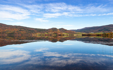 A tranquil mountain lake surrounded by hills reflecting clear skies