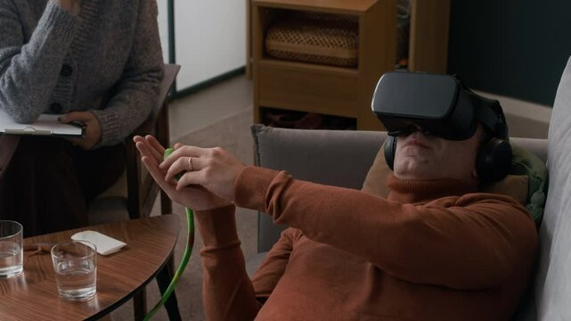Unrecognizable psychologist handing small fake snake to male patient wearing VR headset helping him to overcome phobia of reptiles using modern technology