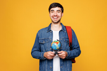 Young smiling boy geography teacher or student he wear denim casual clothes backpack bag hold globe...