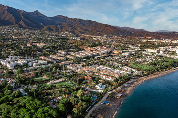 An aerial view of Marbella's vibrant coastline, showing sandy beaches, turquoise sea, luxury resorts, and a backdrop of mountains