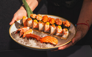 Assorted sushi platter with lobster and salmon garnish held by female hands