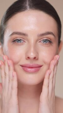 Beautiful Young Woman Touches Her Perfect Face. Natural Cosmetic Skincare Products. Woman demonstrate moisturizing facial care. Elevating Close-up vertical video. Slow motion