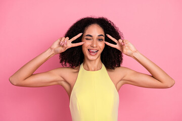 Young stylish woman in yellow dress posing playfully against pink background with cheerful smile...