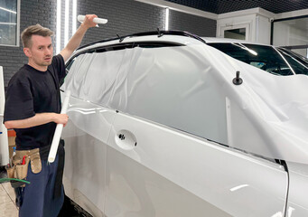 A car wrapping specialist applies a polyurethane film to the car. Detailer smoothes PPF. Car...