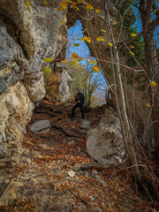 A hiker stands beneath the massive Háromkút Great Rock Arch, a spectacular karst formation surrounded by steep limestone walls and autumn forest.