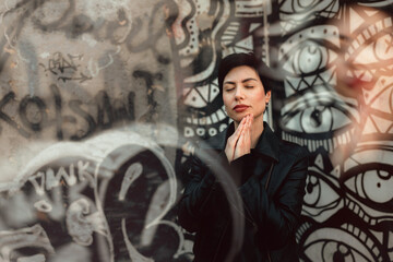 Dreamy young woman with short haircut standing against colorful graffiti wall urban style portrait outdoors