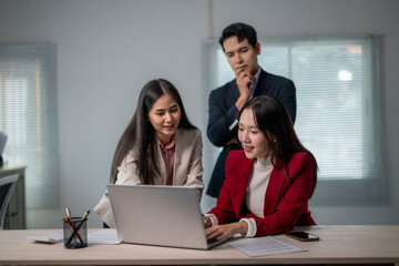Three people are sitting at a desk with a laptop open