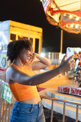 Young woman taking selfie at amusement park with carousel in background