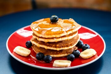 A tall stack of fluffy pancakes with fresh blueberries, syrup, and butter for breakfast.