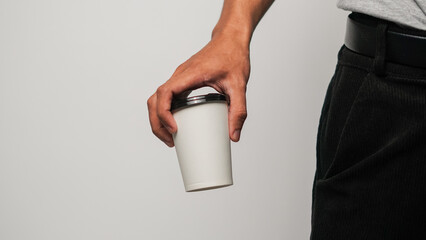 Person's hand holding a minimalist white reusable coffee cup, studio shot on clean background,...