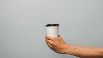 Hand holding white disposable cup with black lid on gray background
