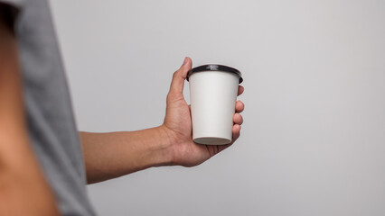 Hand holding blank white disposable coffee cup with black lid against a plain background, ready for...