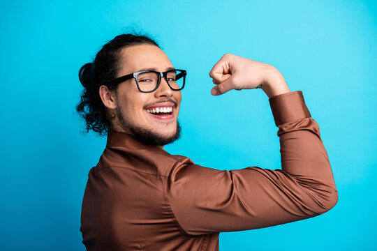 Confident young male professional flexing arm and smiling against blue backdrop