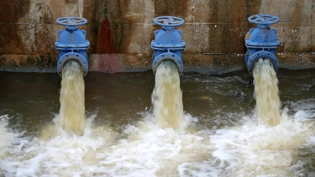 Industrial drainage system with five blue pipes discharging water into a reservoir. Concept of water management, wastewater treatment, and environmental engineering, spillway