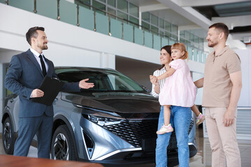 Salesman with clipboard showing new car to happy family in salon