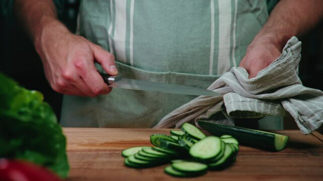 Cinematic close-up of a man cleaning a Japanese knife after slicing a cucumber - slow motion food prep, cooking tutorial, healthy recipes, knife skills.