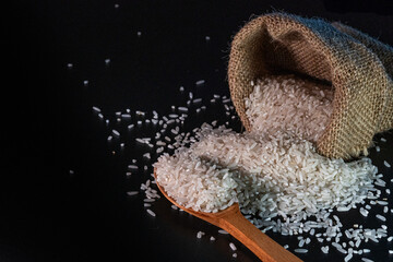 White rice spilling from a burlap sack onto a dark surface, with black background