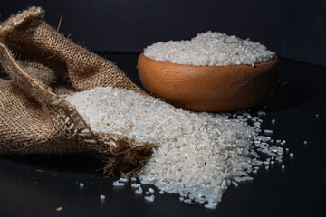 White rice spilling from a burlap sack onto a dark surface, with black background
