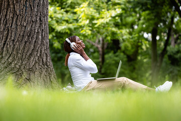 Young black woman with headset enjoy listening to the music in park.