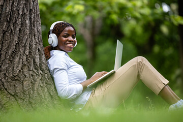 African American female student with laptop computer studying in the park and enjoying nature.
