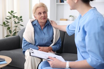 Fototapeta premium Nurse with clipboard examining senior woman indoors, closeup. Home health care service