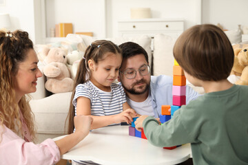 Fototapeta premium Children and their parents building tower with colorful cubes at white table indoors
