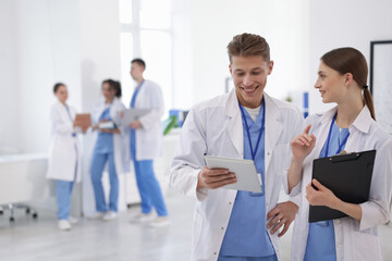 Medical students in uniforms with tablet and clipboard indoors, selective focus