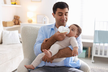 Fototapeta premium Father feeding his little baby with bottle on armchair at home