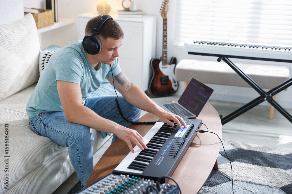 Poster man in headphones working with midi keyboard at table indoors