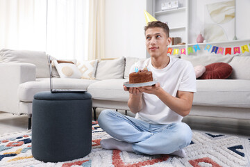 Birthday celebration. Man with cake making wish while having video call via laptop at home