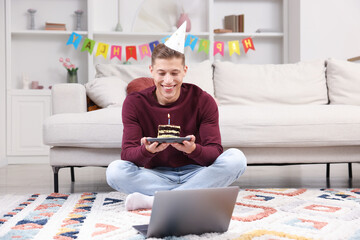 Man with piece of cake celebrating his birthday and having video call via laptop at home