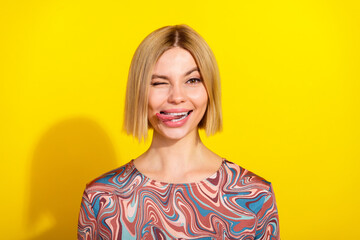 Cheerful young blonde woman playfully winking with a trendy stylish outfit against a vibrant yellow...