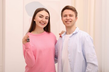 Happy couple with key of their new apartment indoors
