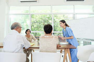 Group of elderly people discussing with female caregiver at a nursing home, reflecting social...
