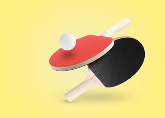 Ping pong rackets and ball in air against yellow background