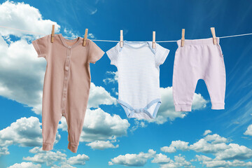 Different baby clothes drying on washing line against blue sky