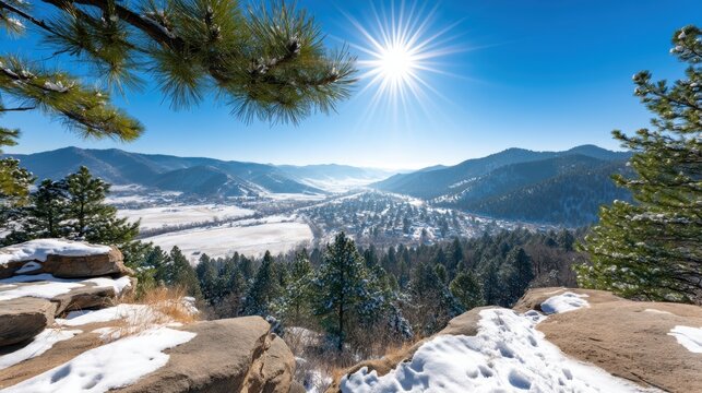 A bright sunny winter day overlooking a snow-covered valley with pine trees and distant mountains beneath a clear blue sky.